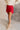 Side view of model wearing the Ruby Red Slit Detail Mini Skort which features red lightweight fabric, slit on the side, red shorts lining, mini length and monochromatic back zipper with hook closure.