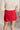 Back view of model wearing the Ruby Red Slit Detail Mini Skort which features red lightweight fabric, slit on the side, red shorts lining, mini length and monochromatic back zipper with hook closure.