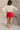 Full body back view of model wearing the Ruby Red Slit Detail Mini Skort which features red lightweight fabric, slit on the side, red shorts lining, mini length and monochromatic back zipper with hook closure.