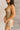 Side view of model wearing the Amber Gold Cowl Neckline Sleeveless Mini Dress which features gold shimmer fabric, mini length, gold lining, a cowl neckline, adjustable straps, and a monochromatic back zipper with a hook closure.