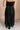 Back view of model wearing the Mila Black Pleated Midi Skirt which features black pleated sheer fabric, black lining, midi length, and an elastic waistband with ruffle details.