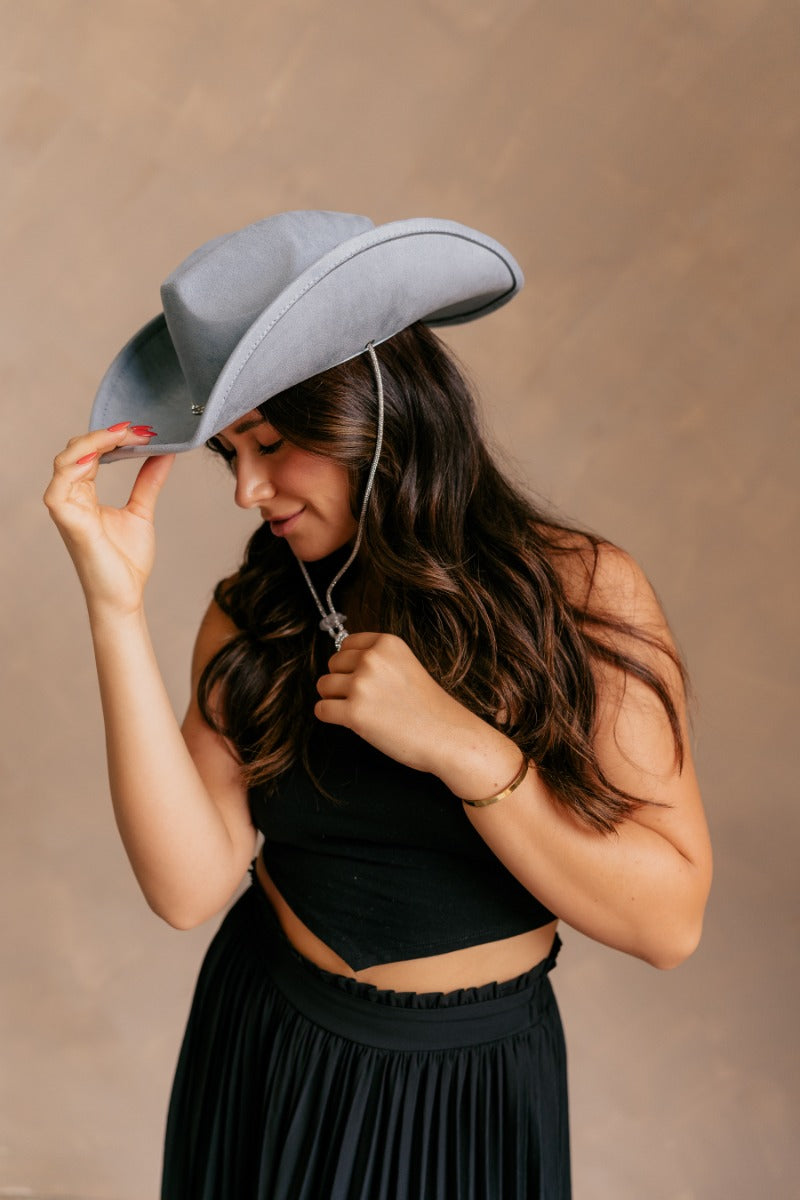 Side view of model wearing the Lainey Blue Rhinestone String Cowgirl Hat features a cowboy shape, dusty blue suede fabric, and a rhinestone covered adjustable string.