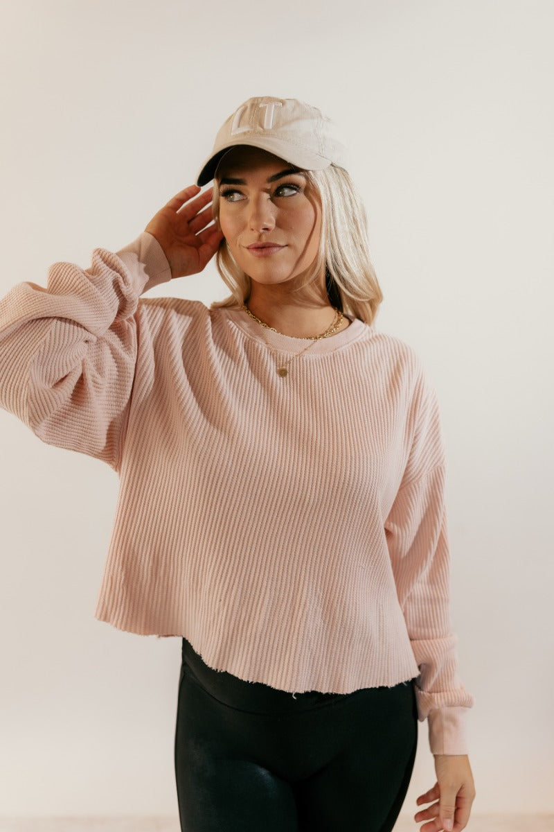 front view of model wearing the Ada Blush Waffle-Knit Long Sleeve Top that has light pink textured fabric, a raw hem, a round neckline, dropped shoulders, and long sleeves with cuffs.