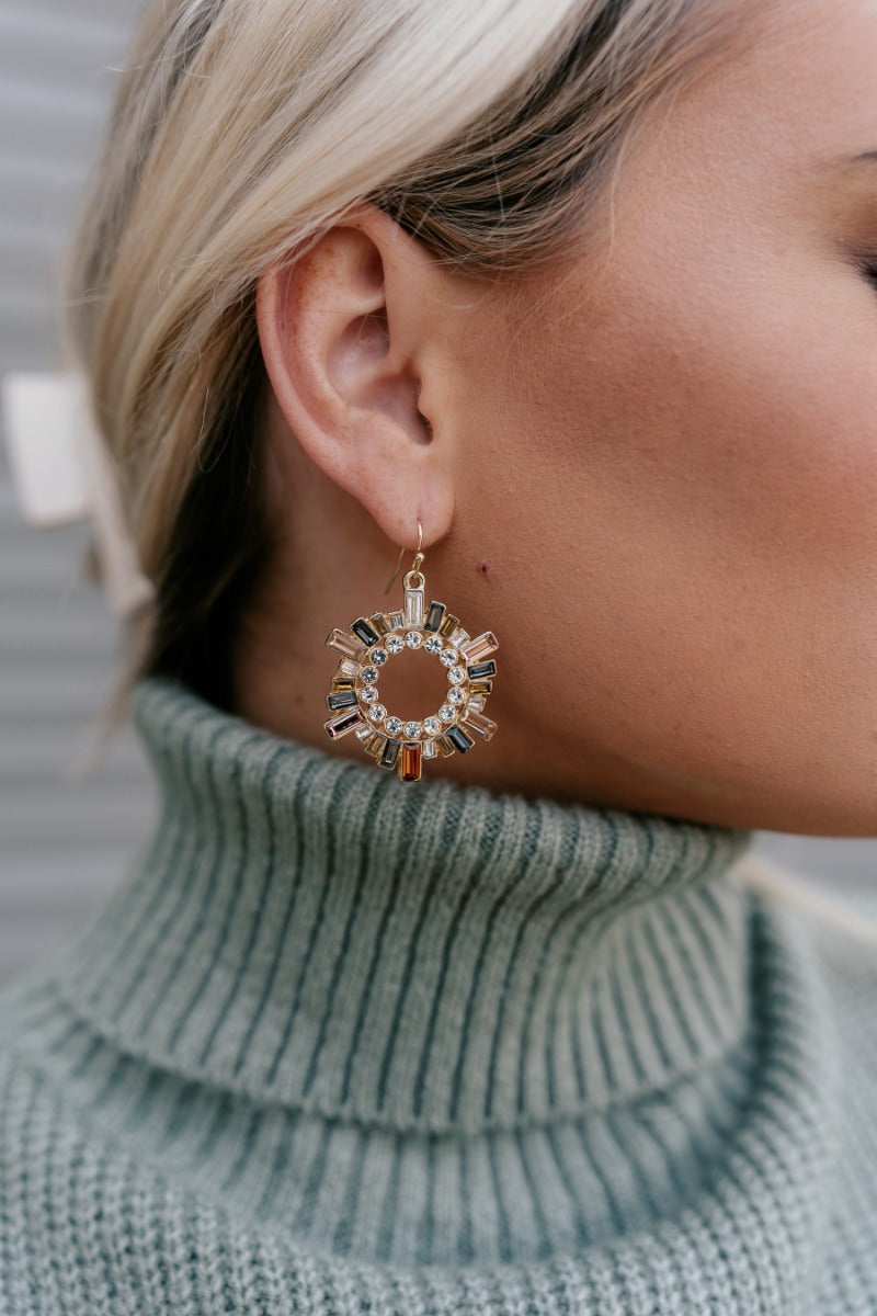 Side view of model wearing the Emma Multi Sunburst Open Circle Earring which features dangle circles with rectangle shaped multi stones and circular clear stones.