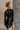 Side view of model wearing the Anastasia Black Embellished Mesh Top that has black mesh fabric, silver embellishments, exposed seam details, a high neckline, and long sleeves.