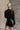Back view of model wearing the Anastasia Black Embellished Mesh Top that has black mesh fabric, silver embellishments, exposed seam details, a high neckline, and long sleeves.