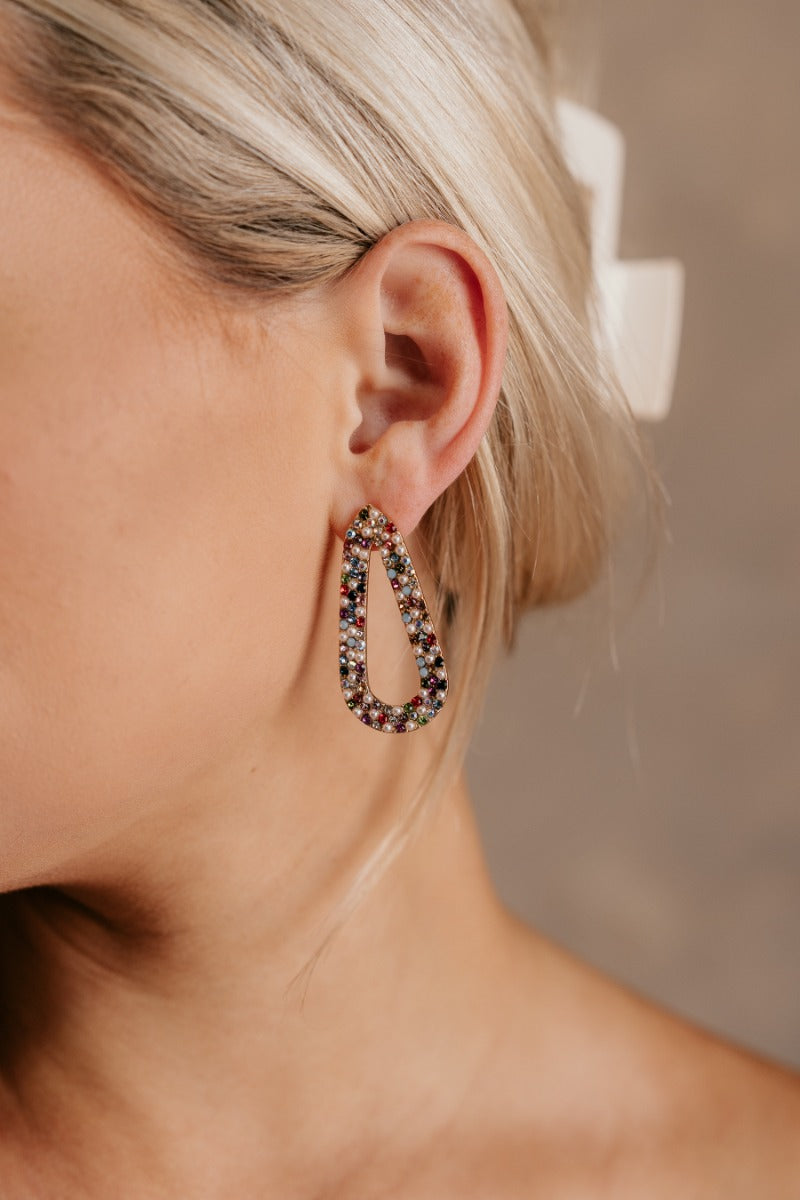 Close up view of model wearing the Jenna Multi & Pearl Beaded Earring which features teardrop shaped filled with pearls and multi color rhinestone design, set in gold.