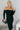 Front view of model wearing the Hayley Black Ribbed Off-The-Shoulder Long Sleeve Midi Dress which features black knit fabric, midi length, a slit in the back, a square neckline, and long sleeves.