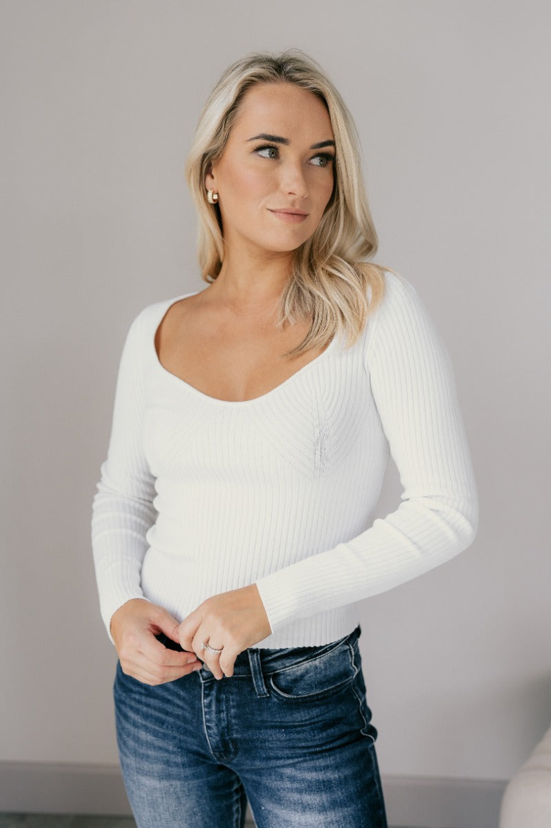 Front view of model wearing the Ember Off White Long Sleeve Ribbed Top which features off white ribbed fabric, a sweetheart neckline, and long sleeves.