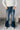 Front view of model wearing the Rooted Denim: Leah Dark Wash Flare Leg Jeans which features dark wash denim fabric, a front zipper with a button closure, two front pockets, two back pockets, belt loops, and flared legs with fray hem.