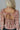 Back view of model wearing the Elliana Pink Floral Long Sleeve Top that has a rust, pink, tan and cream floral print, lace details, a v-neck, an open back with a tie , and long puff sleeves.