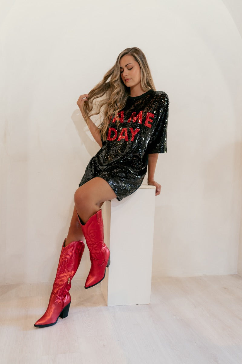 Frontal view of model wearing the Game Day Red & Black Sequin Dress that has black sequins, red sequins that say "Game Day", and black knit back, an oversized fit, short sleeves, and a round neck.