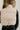 Back view of model wearing the Tahoe Cream Faux Leather Puffer Cropped Vest which features cream faux leather puffer fabric, a cropped waistline with a drawstring, a front zip-up closure, two front pockets, and a high neckline.
