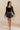 Full body view of model wearing the Piana Washed Black Denim Mini Skirt which features washed black denim fabric, mini length, an overlap design with frayed hem, two front snap closures, one front pocket with a snap cloure and an adjustable strap, and a m