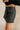 Side view of model wearing the Piana Washed Black Denim Mini Skirt which features washed black denim fabric, mini length, an overlap design with frayed hem, two front snap closures, one front pocket with a snap cloure and an adjustable strap, and a monoch