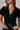 Close up view of model wearing the Rielle Black Adjustable Belt Short Sleeve Jumpsuit which features black fabric, two front pockets, a front zipper, an adjustable belt with a silver buckle, a collared neckline, short sleeves, and straight pant legs.