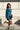Frontal view of model wearing The Elaine Satin Dress features a blue, green satin material, a cowl neckline, long sleeves, an open cowl back with a tie closure, and a mini length.
