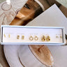 Top view of the New Chapter Earring Set, packaged in a white box with "Girls night, everyday, date night, everyday, and weekend" text. It includes 5 pairs of gold stud earrings, featuring circles and rectangles with rhinestones, bars, and double hoops.