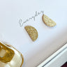 Close-up image of the everyday earrings, which are gold glitter half-moon studs.