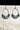 Front view of the Flower Power Earrings in sage, which feature white arches with crescent pendants, with a green floral pattern.