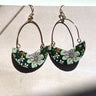Front view of the Flower Power Earrings in sage, which feature white arches with crescent pendants, with a green floral pattern.