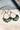 Top view of the Flower Power Earrings in sage, which feature white arches with crescent pendants, with a green floral pattern.