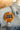 Close up image of the Touch Down Button in Gold features a mustard button with beige and orange. Text says "TOUCH DOWN" in black. Button is pinned to a denim jacket.