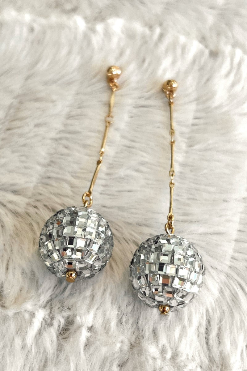 Close-up image of the Disco Fever Earrings, that feature gold chain links with large clear stone balls.