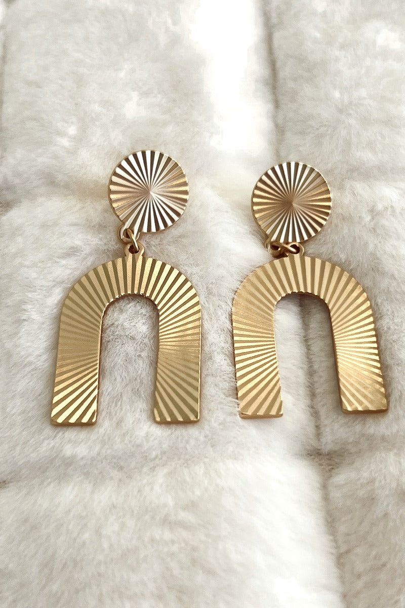 Close image of the New You Earrings that feature matte gold horseshoe-shaped pendants with pleated details.