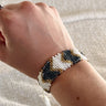 Image of model's wrist; model is wearing the Gold Rush Beaded Bracelet that features white, black, and gold beading with an adjustable white tasseled tie.
