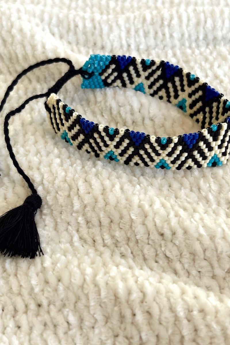 Close image of the Forever Yours Beaded Bracelet that features black, white, and blue beading with an adjustable black tasseled tie.