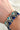 Close image of the Forever Yours Beaded Bracelet that features black, white, and blue beading with an adjustable black tasseled tie.. Shown on model's wrist.