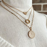 Front view of the Piece of Me Necklace which features triple skinny chain layer with three gold medallion attachments.
