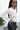 Side view of model wearing the New Rhythm Top, that has cream and beige fabric with a dimensional pattern, ruching ties on the hem, a round neckline and long sleeves.