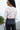Back view of model wearing the New Rhythm Top, that has cream and beige fabric with a dimensional pattern, ruching ties on the hem, a round neckline and long sleeves.