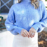 Front view of model wearing the You And Me Sweater, that has blue knit fabric with stitched details, a high neckline, and balloon sleeves with fitted wrists. Sweater is styled tucked up.