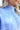 Close-up neckline view; model is wearing the You And Me Sweater, that has blue knit fabric with stitched details, a high neckline, and balloon sleeves with fitted wrists. Sweater is styled tucked up.