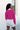 Back view of model wearing the Future Is Bright Sweater in Pink, that has hot pink ribbed knit fabric, a cropped waist, a round neckline, and balloon sleeves with cuffed wrists