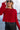 Close up view of model wearing the Always A Hit Sweater which features red ribbed knit fabric, a cropped waist, a round neckline and balloon sleeves with cuffed wrists.