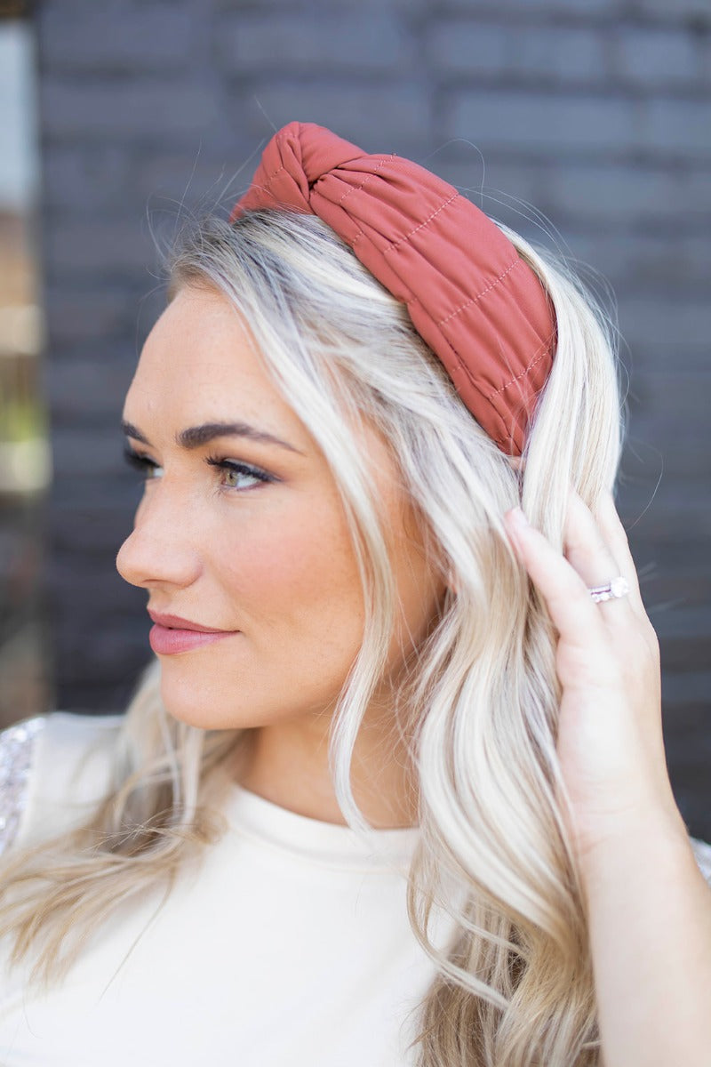 Side view of model wearing the Sadie Headband in Rust, which features a structured band with a satin lining and a quilted exterior with a top twist.