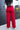 Full body back view of model wearing the Endless Love Pant which features red satin fabric, geometric pattern, zipper and hook closure, two back pockets, belt loops and straight wide leg.