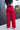 Full body back view of model wearing the Endless Love Pant which features red satin fabric, geometric pattern, zipper and hook closure, two back pockets, belt loops and straight wide leg.