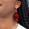 Close up view of model wearing the Let's Party Earrings in Red which features red metallic tassels. 