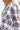 Side view of model wearing the Harvest Dreams Flannel which features brown, black and cream fabric with a plaid pattern, a button-up front with tortoise buttons, one pocket on the left chest, a collared neckline, a high-low hemline with small slits, and l