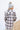 Back view of model wearing the Harvest Dreams Flannel which features brown, black and cream fabric with a plaid pattern, a button-up front with tortoise buttons, one pocket on the left chest, a collared neckline, a high-low hemline with small slits, and l