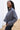 Side view of model wearing the Greater Days Sweatshirt which features grey fabric, distressed detailing with front zip up, one pocket, a cropped waist, a high neckline, and long sleeves with distressed wrists.