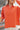 Close up view of model wearing the Breezy Top In Orange which features orange fabric, silver button clasps, collared neckline, distressed hemline and details, dropped shoulder and long sleeves.