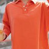 Close up view of model wearing the Breezy Top In Orange which features orange fabric, silver button clasps, collared neckline, distressed hemline and details, dropped shoulder and long sleeves.