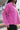 Side view of model wearing the Breezy Top In Magenta features magenta washed fabric, silver button clasps, collared neckline, distressed hemline and details, dropped shoulder and long sleeves.