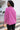 Back view of model wearing the Breezy Top In Magenta features magenta washed fabric, silver button clasps, collared neckline, distressed hemline and details, dropped shoulder and long sleeves.